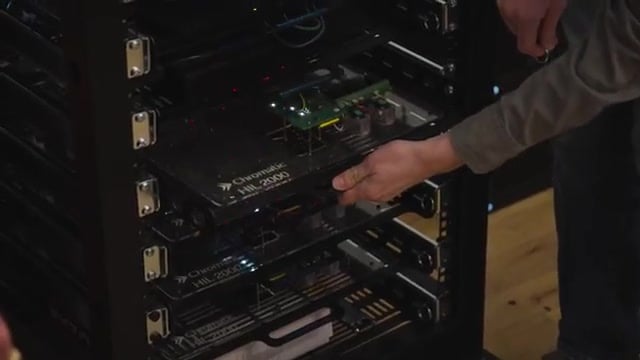 A technician sliding a Chromatic HIL 2000 hardware-in-the-loop test tray into a rack of Fortell hearing-aid test boards
