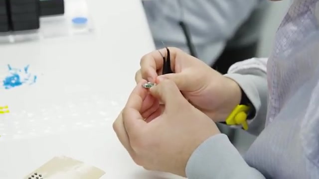 Close-up of a technician using tweezers and an ESD wrist strap to handle a tiny Fortell hearing-aid component
